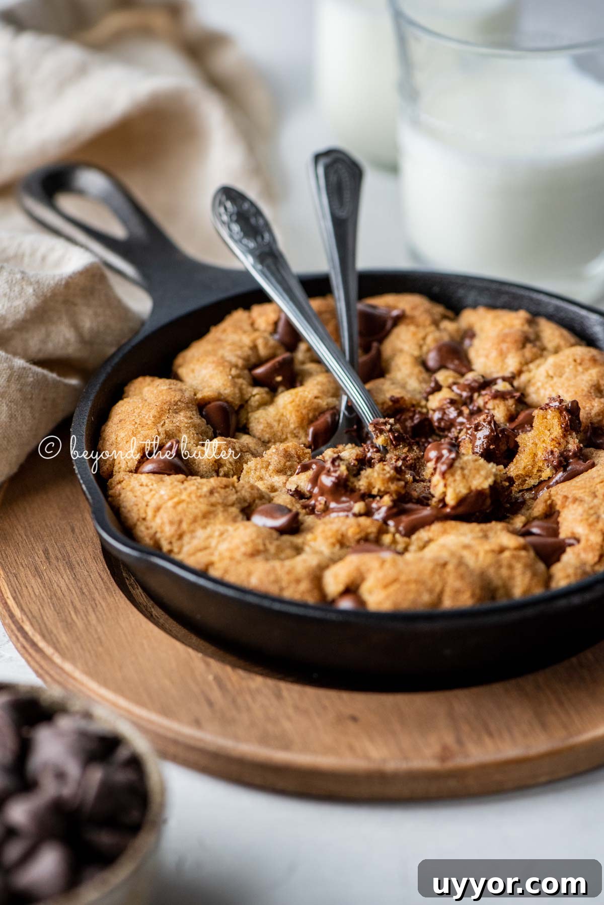 Warm brown butter chocolate chip skillet cookie with two spoons resting in skillet on wood trivet | All Images © Beyond the Butter®