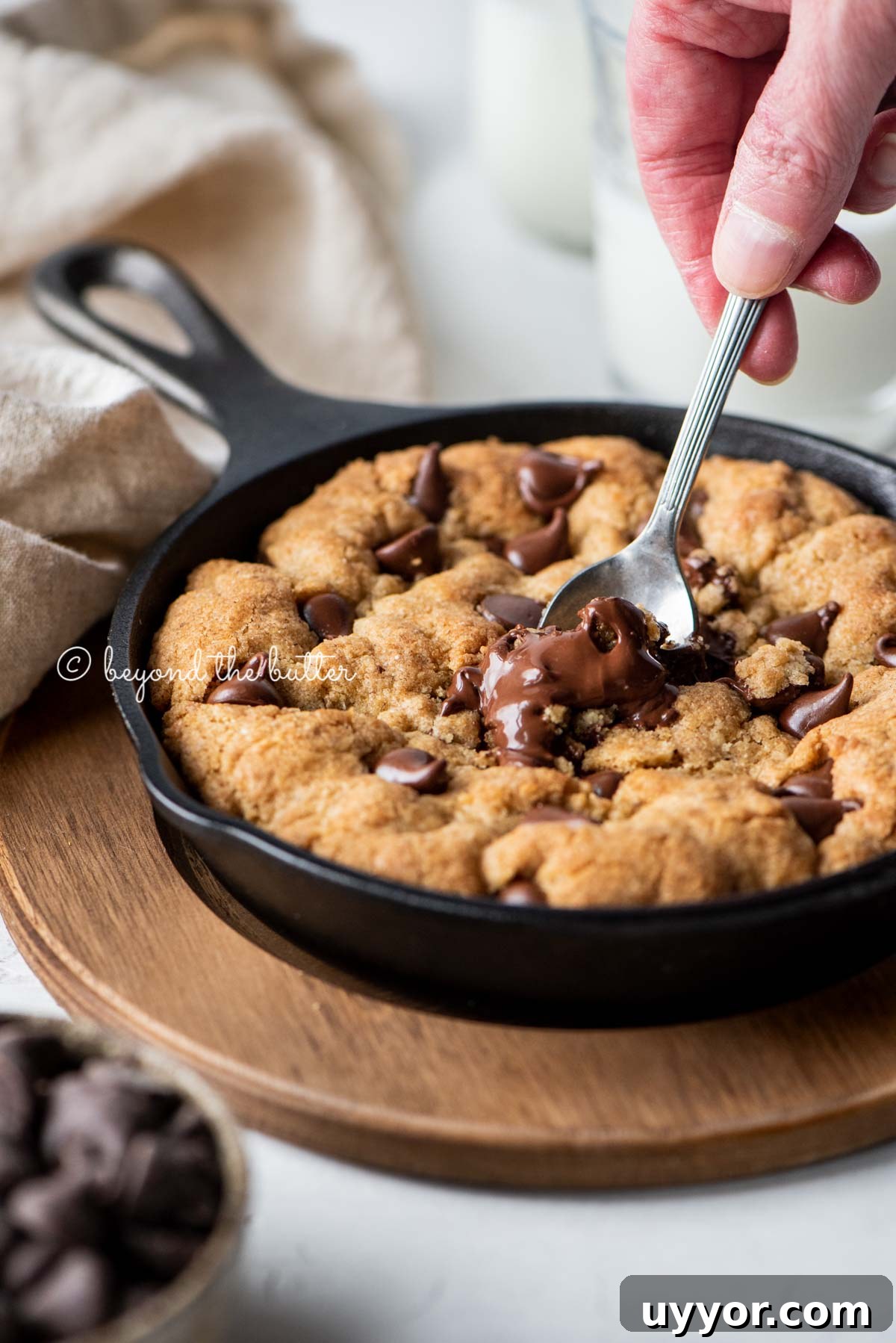 Warm brown butter chocolate chip skillet cookie with two spoons resting in skillet on wood trivet | All Images © Beyond the Butter®