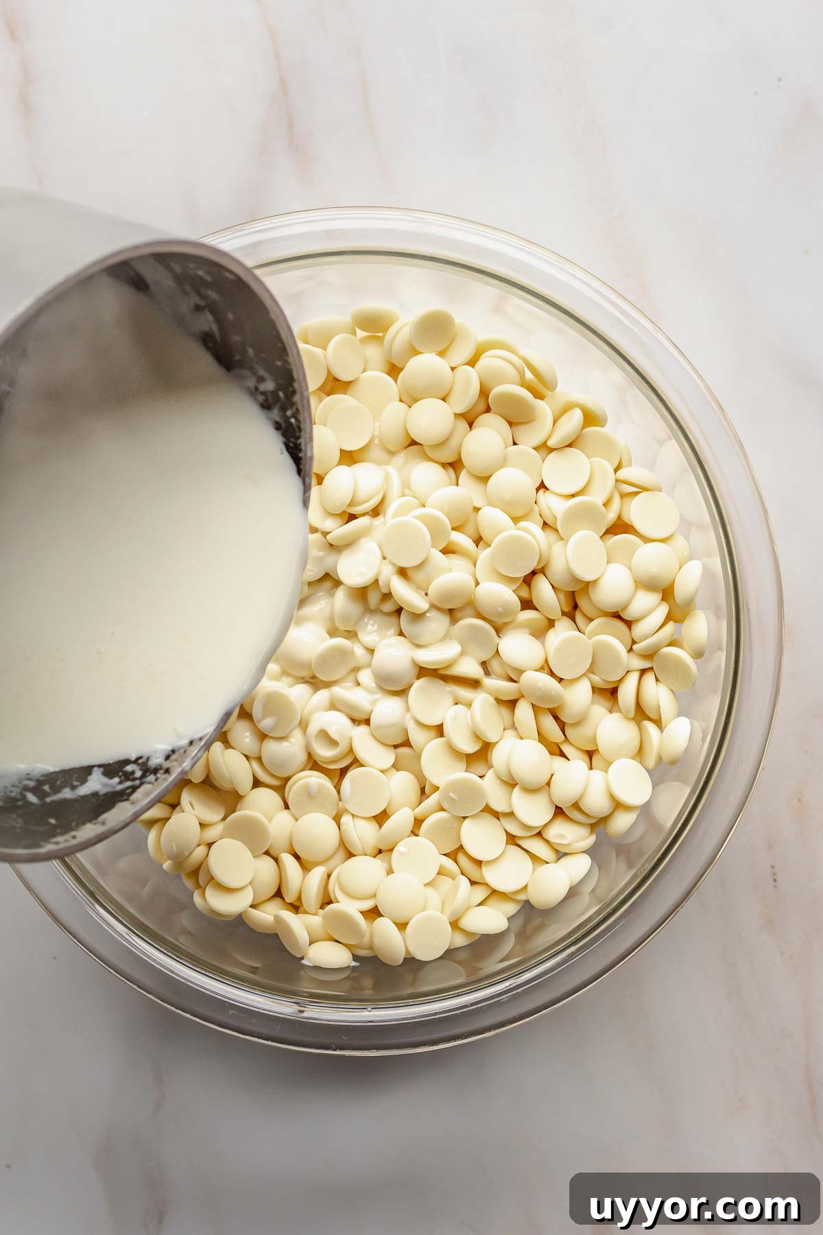 Steaming heavy cream pouring onto white chocolate in a bowl.