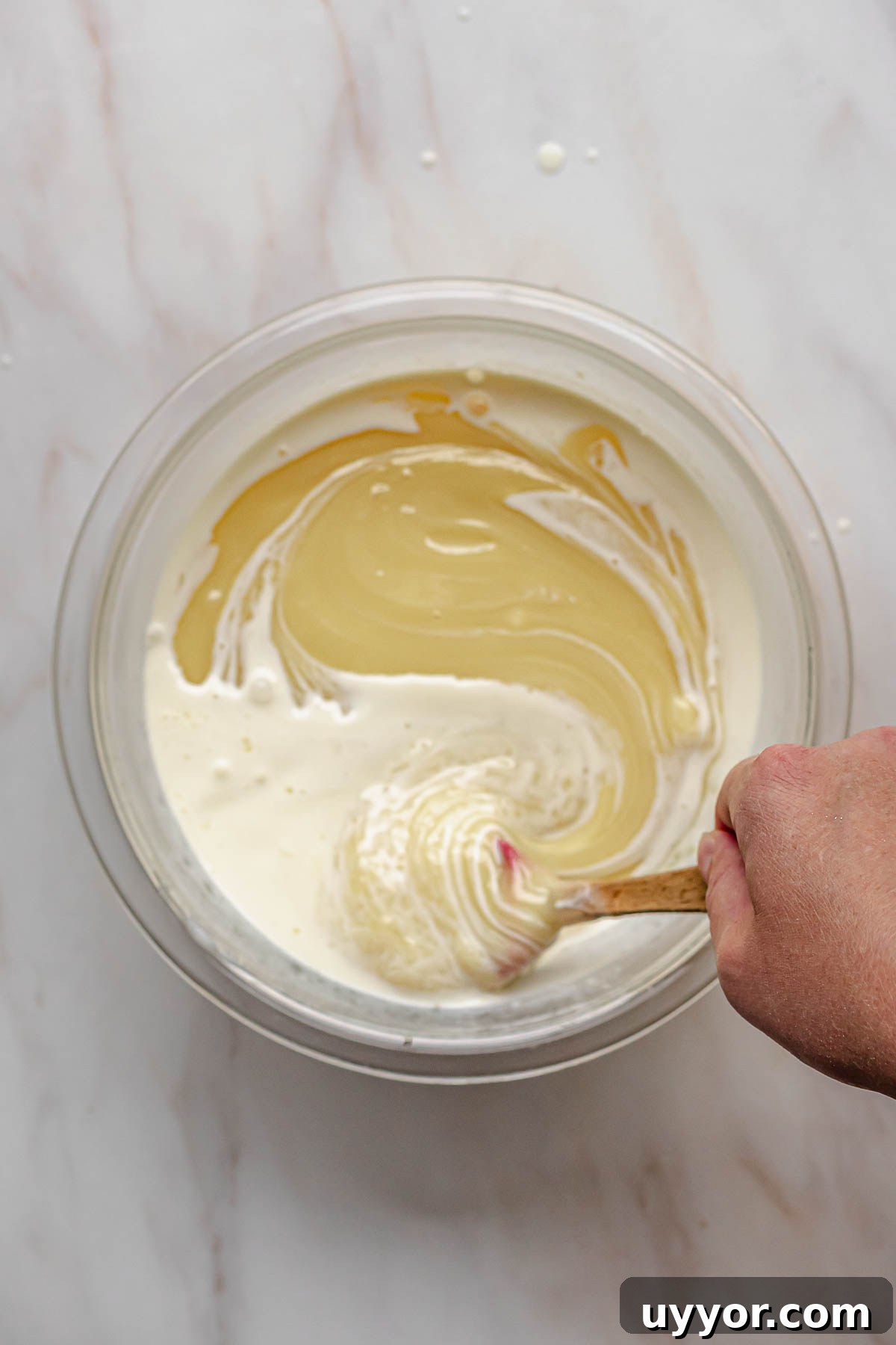 A hand mixes together melted white chocolate and heavy cream.