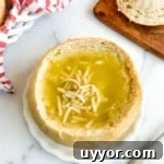 Sourdough bread bowl filled with soup on a white plate on a white background.