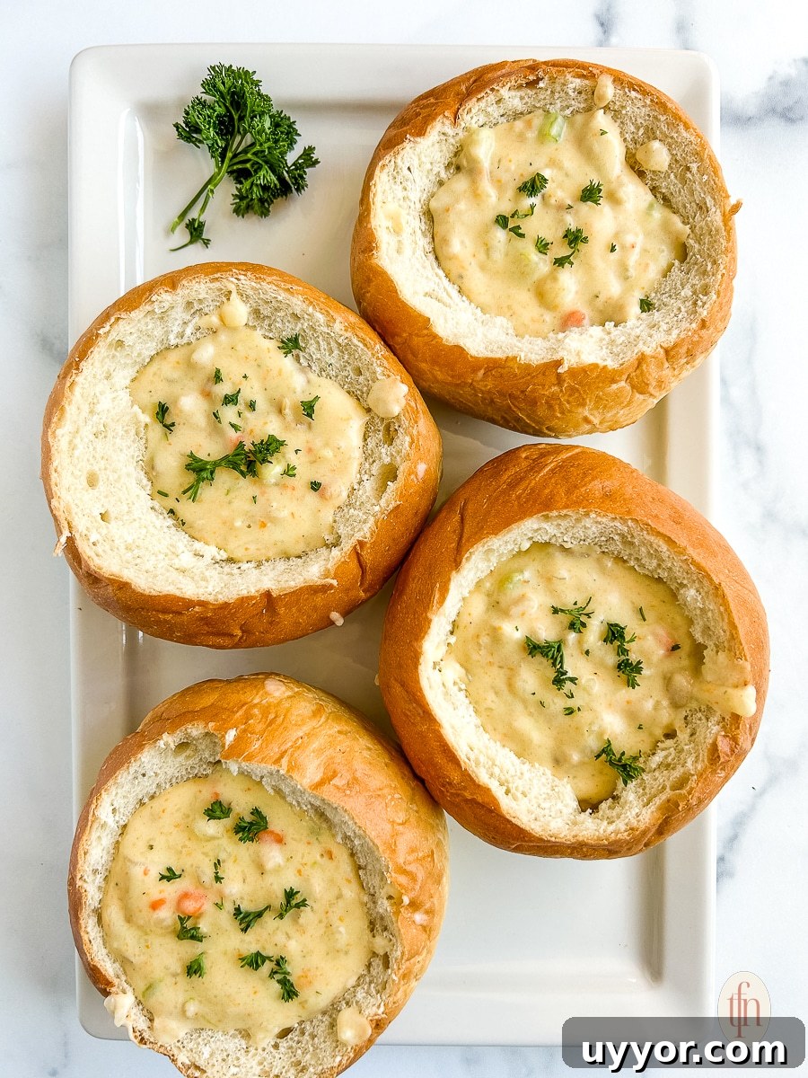 Four bread bowls filled with creamy soup garnished with fresh herbs, sitting on a white platter.