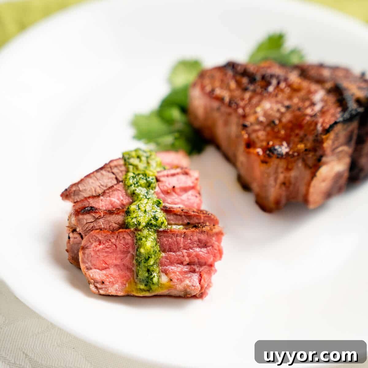 Sliced lamb with a drizzle of pesto in front of an uncut lamb chop