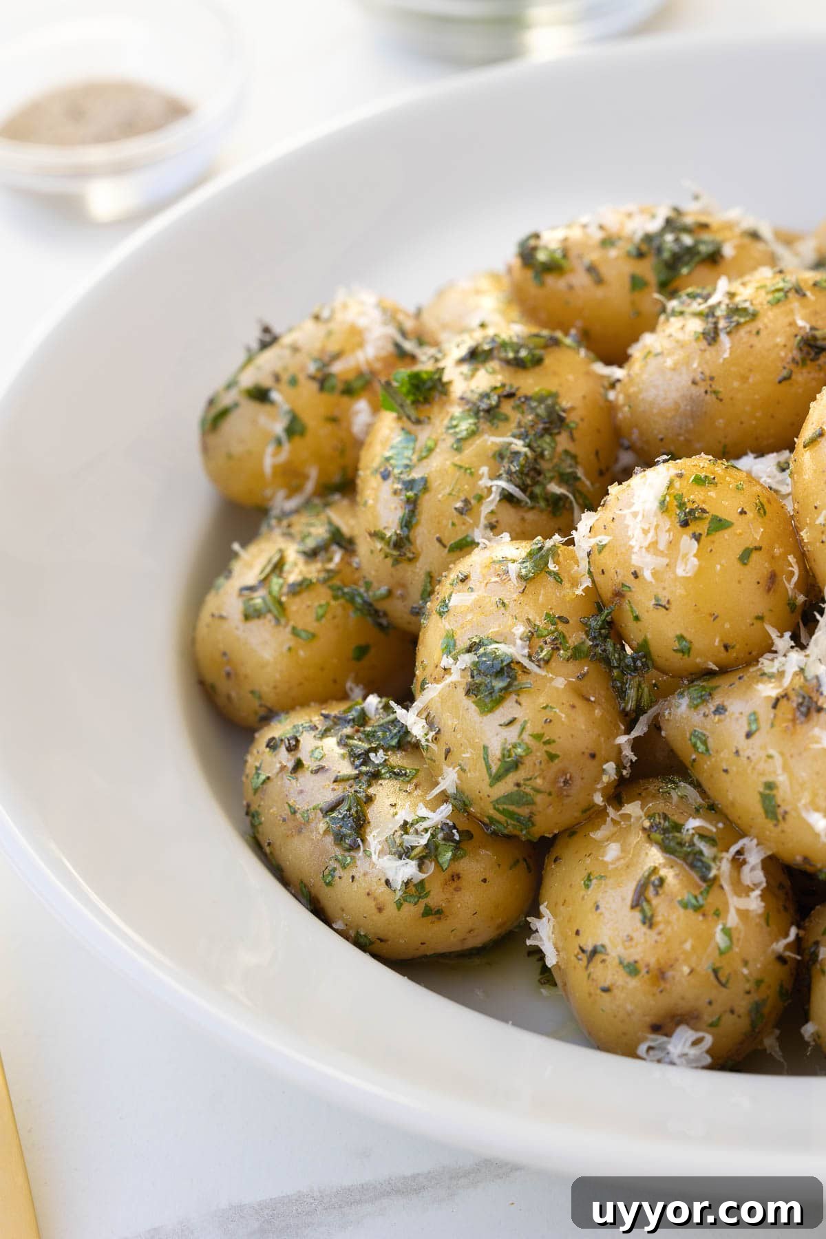 Buttery Baby Dutch Yellow Potatoes Recipe for Tender Roasted Spuds 8 At the table, a white bowl of golden herbed baby Dutch potatoes wtih herbs and Parmesan.