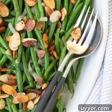 A bowl of bright green beans almondine with toasted buttered almonds.