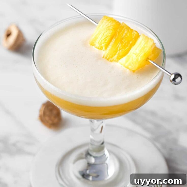 A pineapple whiskey sour garnished with pineapple chunks.