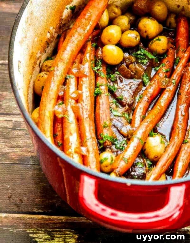 Balsamic Dijon Chuck Roast: Flavorful Pot Roast Recipe 4 Angled shot of a red Dutch oven filled with chuck roast, carrots, and potatoes on a rustic wooden table