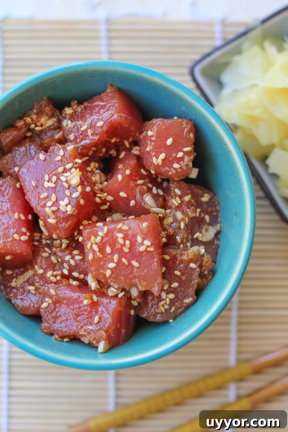 Ahi Poke in a teal bowl with a small bowl of pickled ginger to the side with chopsticks. Ready to eat.