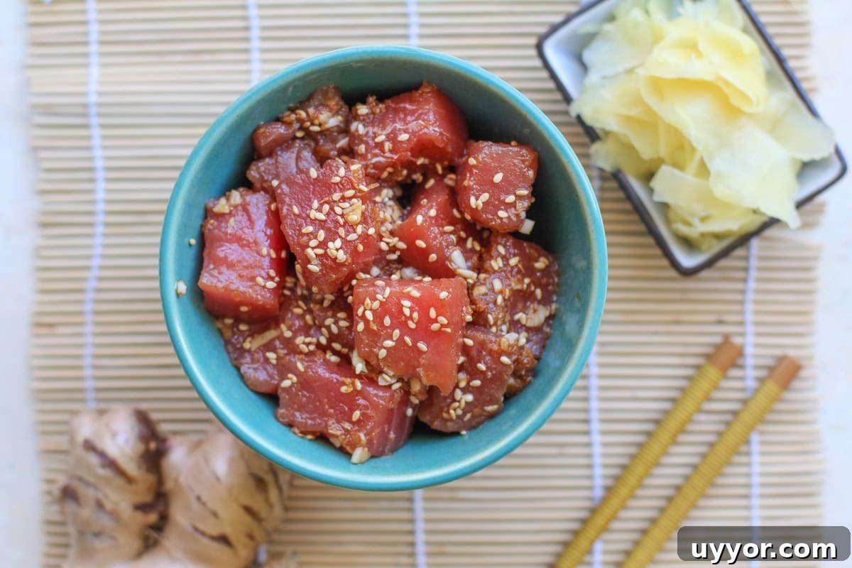 Bowl of ahi poke sprinkled with sesame seeds. Fresh ginger and chop sticks to the side.