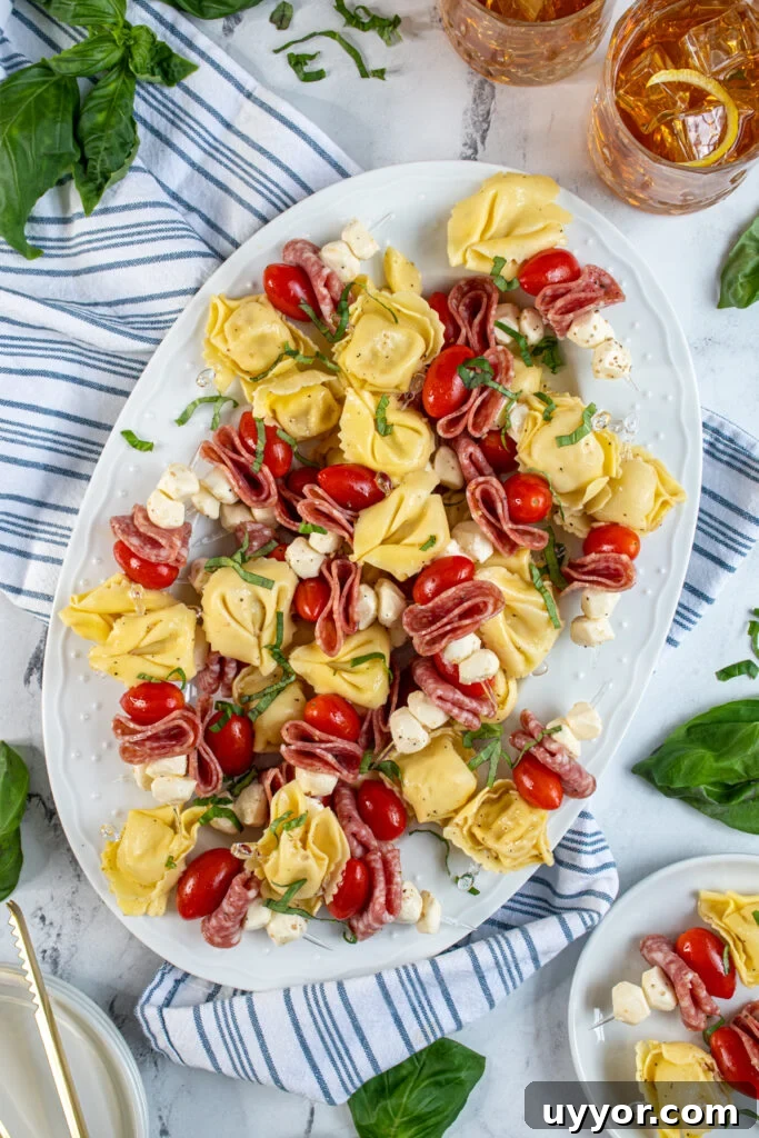 Tortellini Skewers: Bite-Sized Appetizer with Pesto and Cherry Tomatoes 3 A large white platter filled with colorful tortellini skewers and garnished with basil.