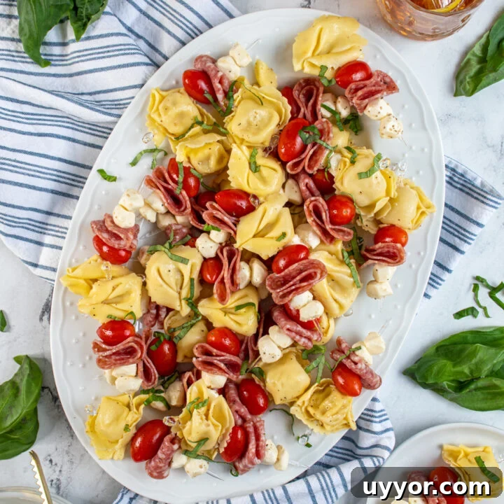A platter surrounded by plates and fresh basil filled with tortellini skewers.