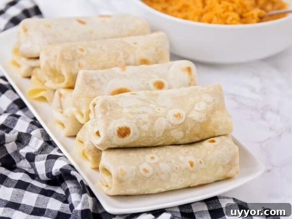 Several bean burritos stacked on a white plate.