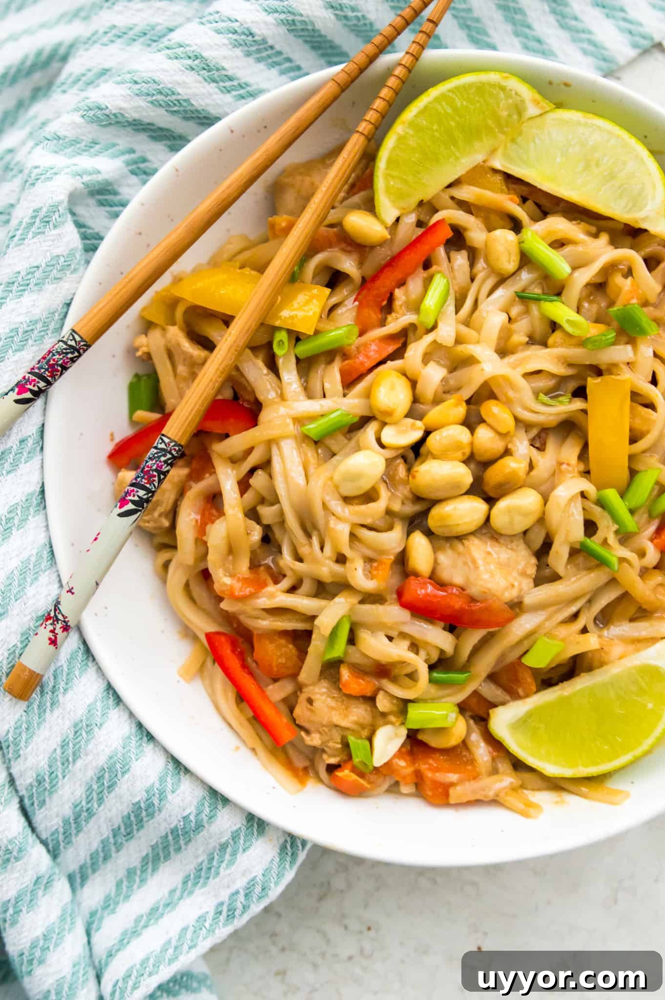 A bowl of Instant Pot Pad Thai garnished with lime wedges and peanuts. 