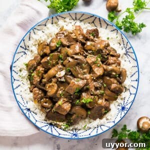 Instant Pot Beef Tips with Rich Mushroom Gravy 14 An overhead image of a blue and white bowl of beef tips over rice with parsley and mushrooms around it.