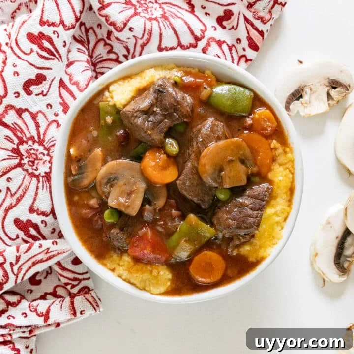 An overhead image of beef stew in a bowl of polenta with a napkin near it and mushrooms.