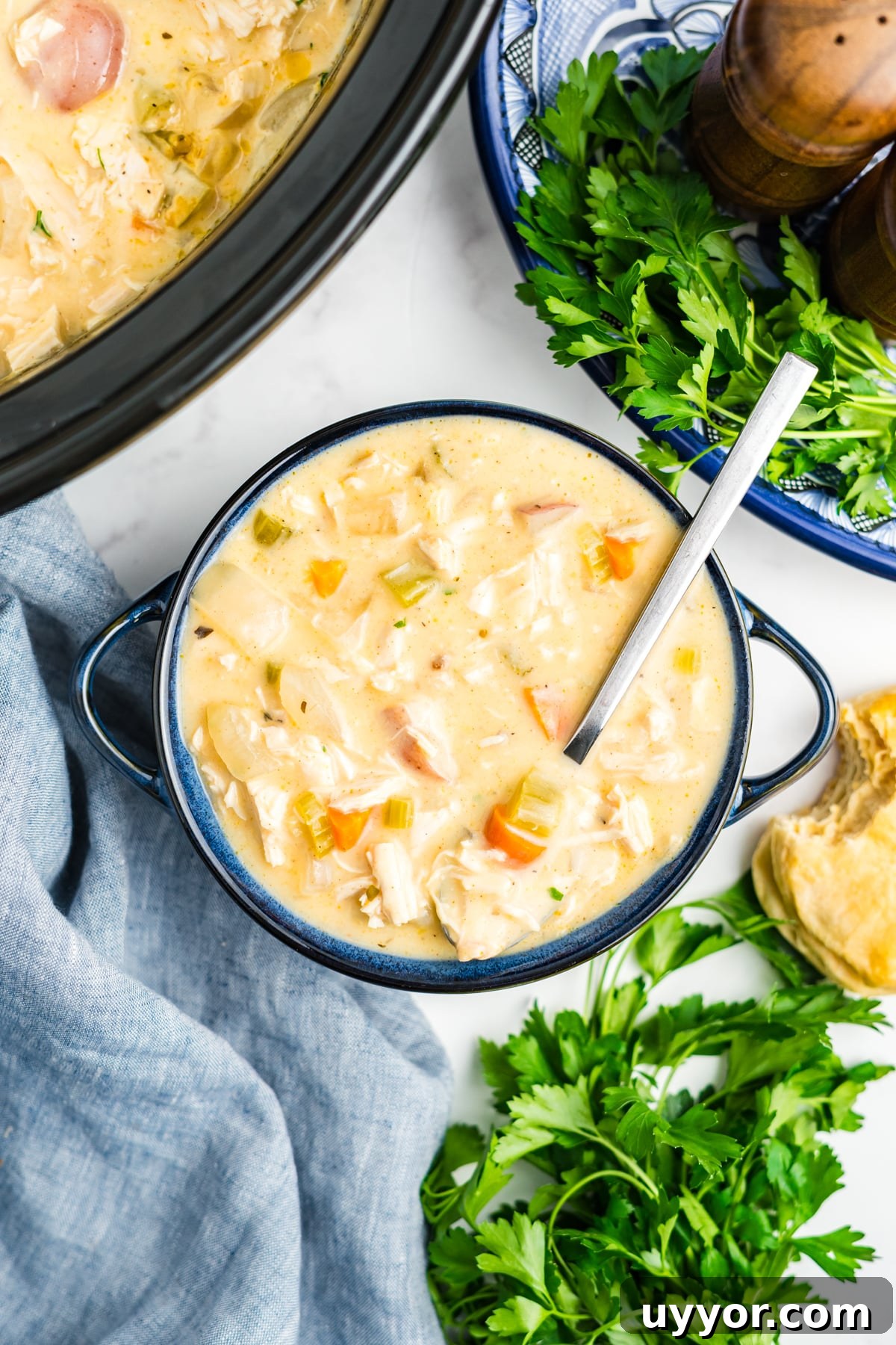 A blue soup bowl of slow cooker chicken stew with a spoon resting in the bowl.