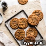 Ginger cookies on a baking sheet resting on a brown parchment paper rectangle. A jar of molasses is nearby.