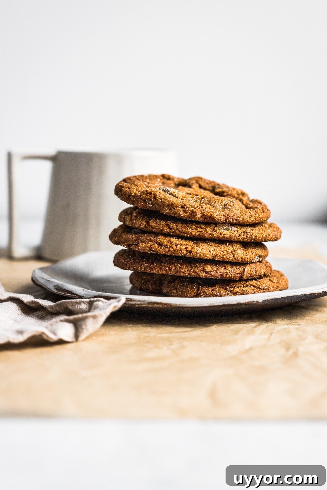 Side view of 5 ginger molasses cookies stacked on a plate with a cup of tea in background