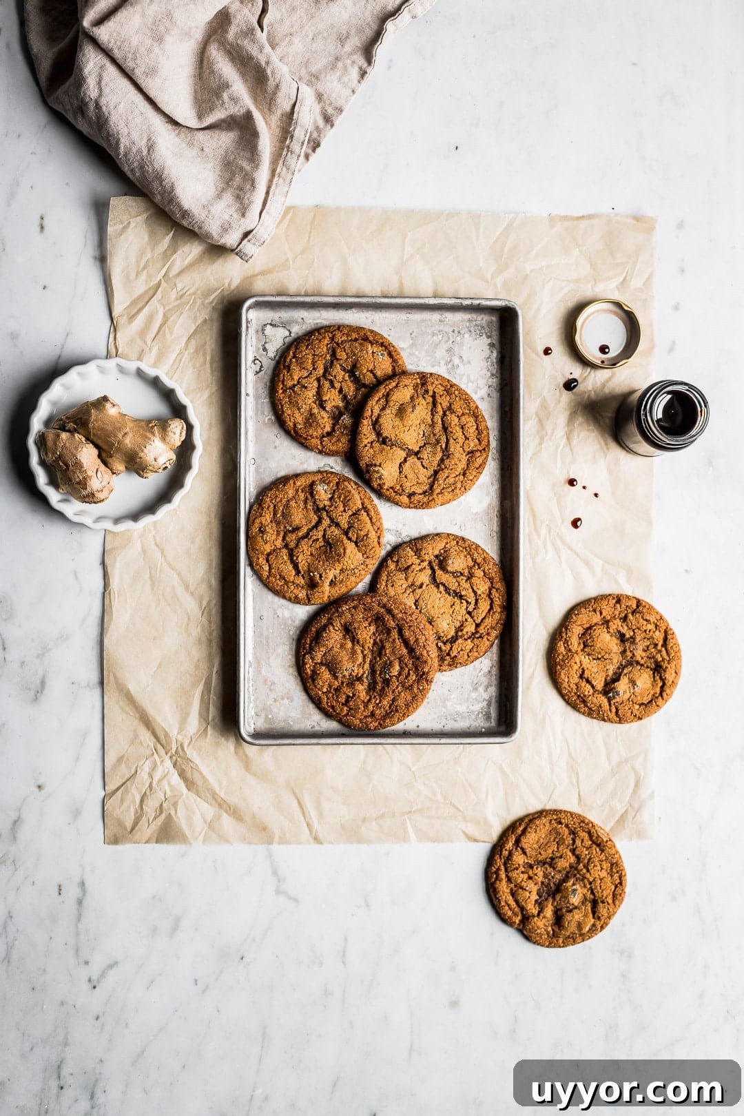 Top view of cookies on small baking sheet with ginger and molasses nearby on white marble background