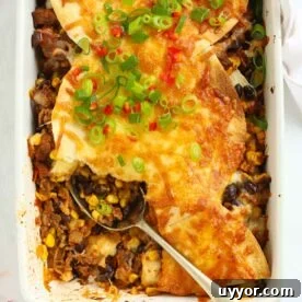 Looking down on an oven dish filled with Mexican beef with sweetcorn and beans, topped with tortillas and cheese, with a spoon dishing out.