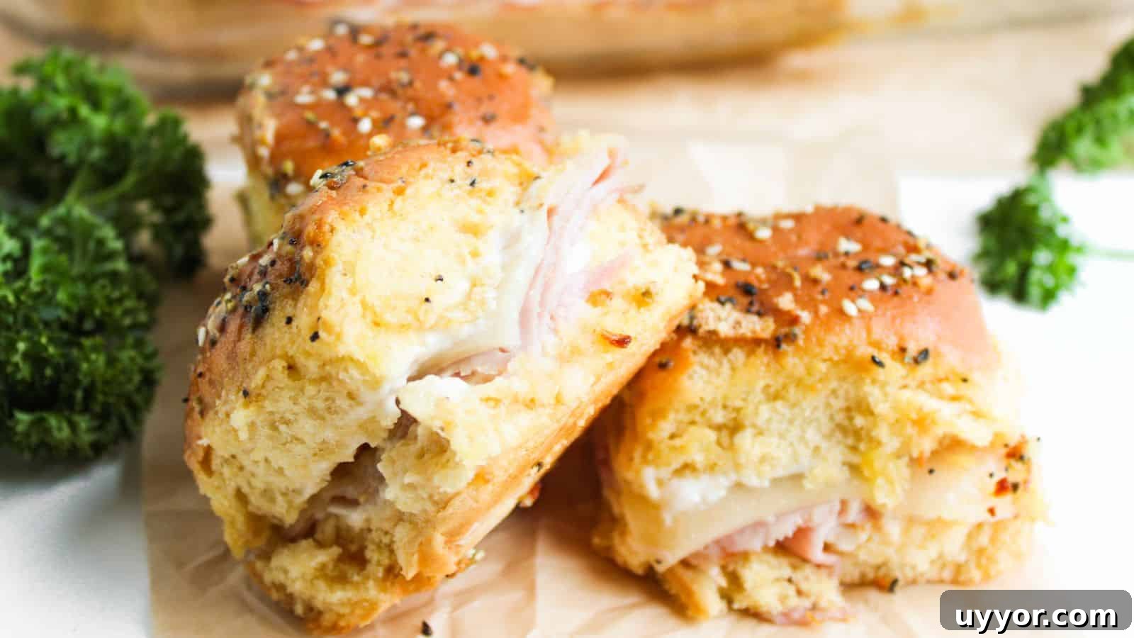 Three ham and cheese sliders on seeded buns are placed on parchment paper. Bright green parsley is visible in the background.