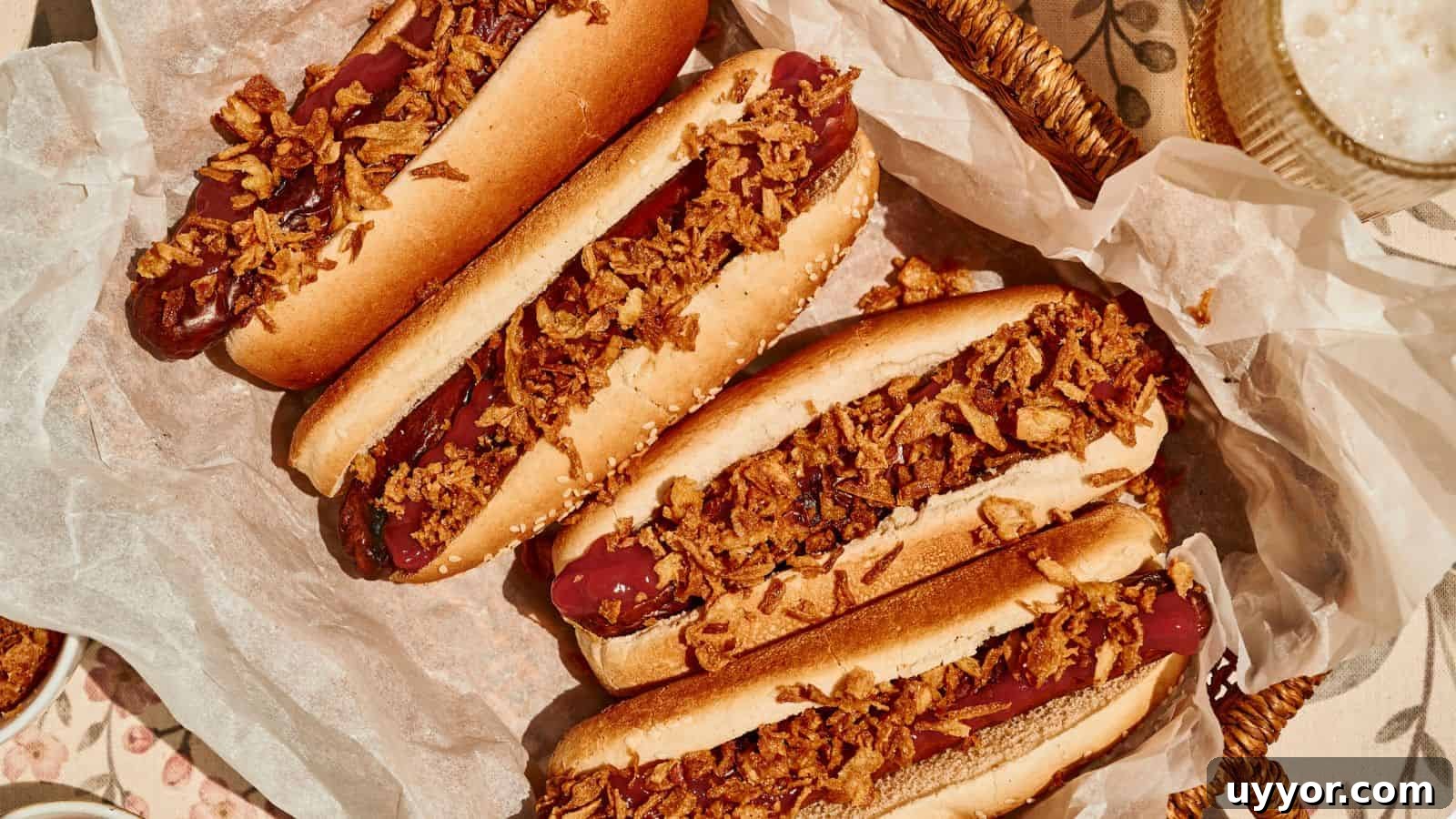 Four hot dogs in buns topped with crispy fried onions are arranged on parchment paper in a basket.