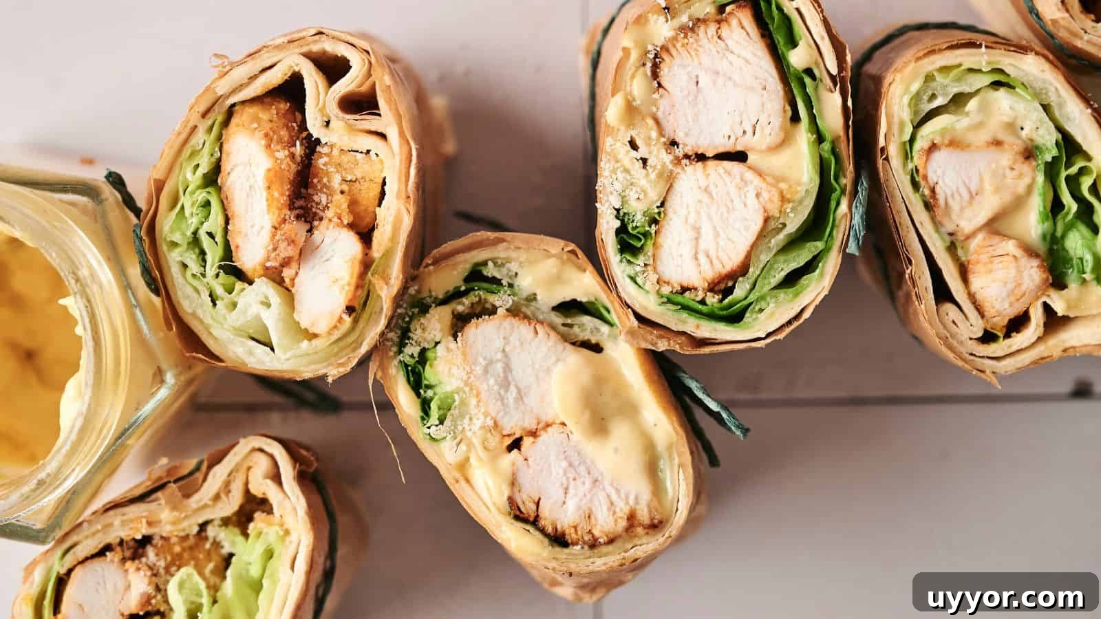 Close-up of sliced chicken wraps with lettuce, cheese, and a creamy sauce, next to an open jar of mustard on a wooden surface.