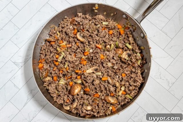Ground beef with carrots and mushrooms cooking in a skillet.
