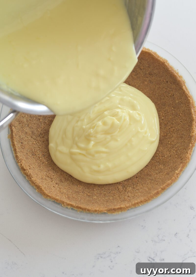 Lemon custard is being poured onto a prepared graham cookie pie crust.