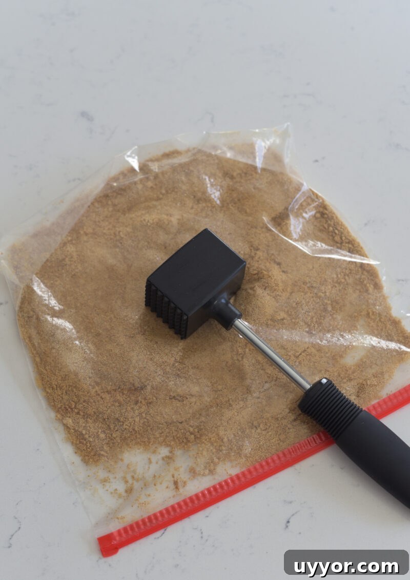 A meat hammer is crushing graham cookie crackers in a zip bag.