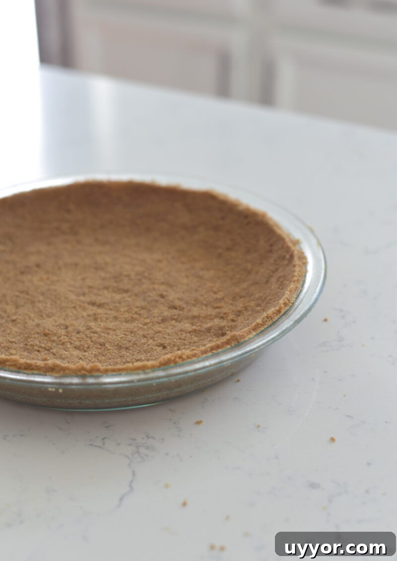 Graham cookie crumbs are pressed onto a pie dish.