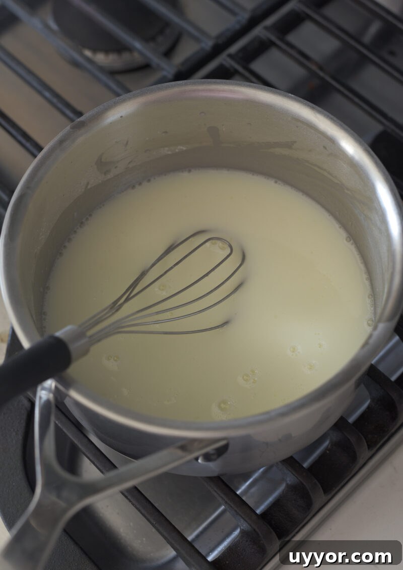 A flat whisk is stirring the lemon sugar mixture in a pan on the stove.