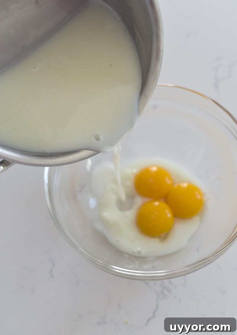 Hot lemon milk mixture is slowly poured on egg yolks in a bowl.