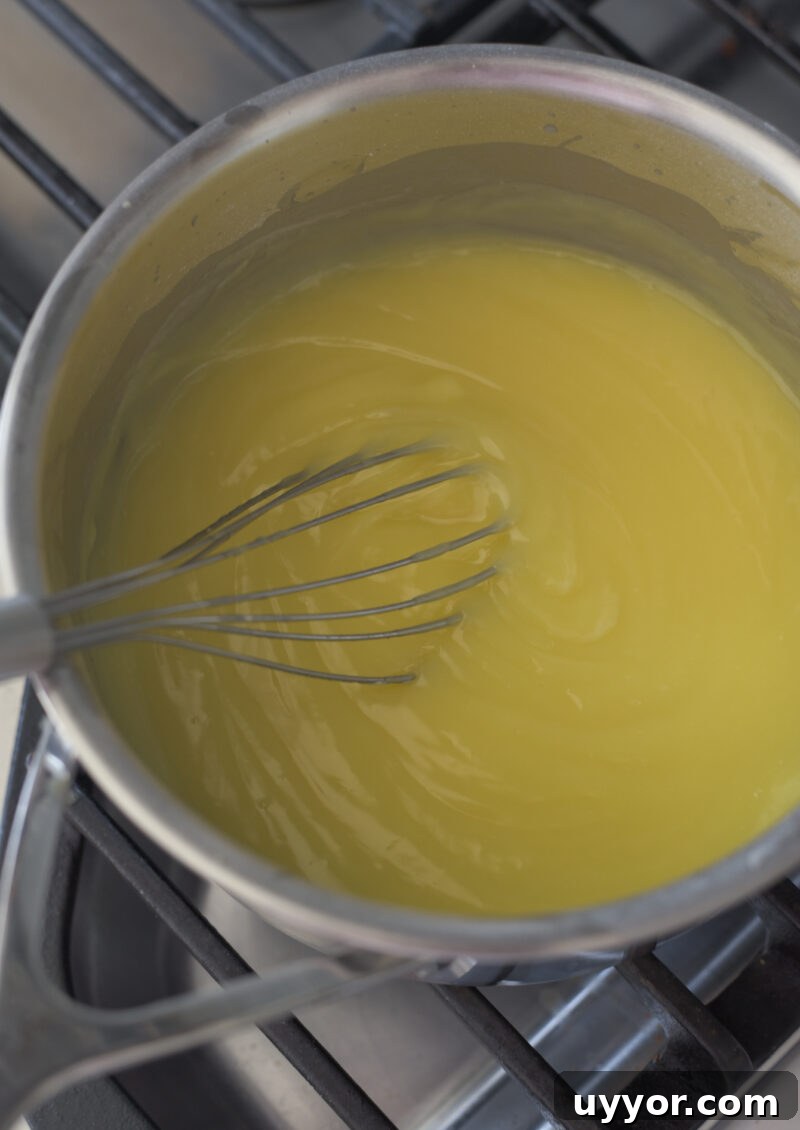 A whisk is stirring the lemon custard until thickened in a pan on the stove.