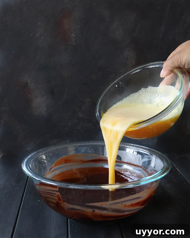 Spicy Chocolate Lava Cakes with Molten Centers 10 Pouring egg and sugar mixture into a glass mixing bowl filled with melted chocolate mixture