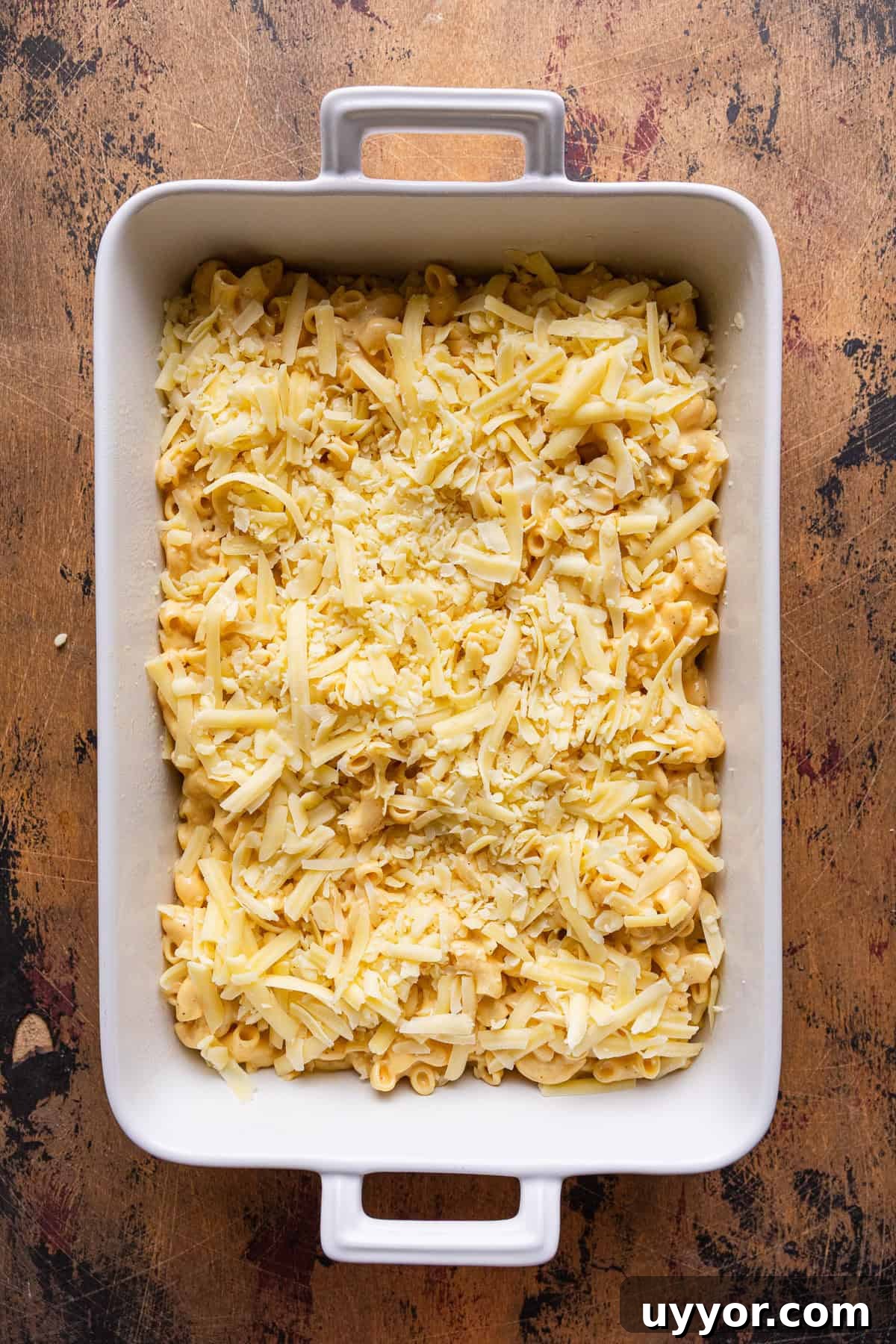 Shredded cheese layered on top of mac and cheese in a baking dish.