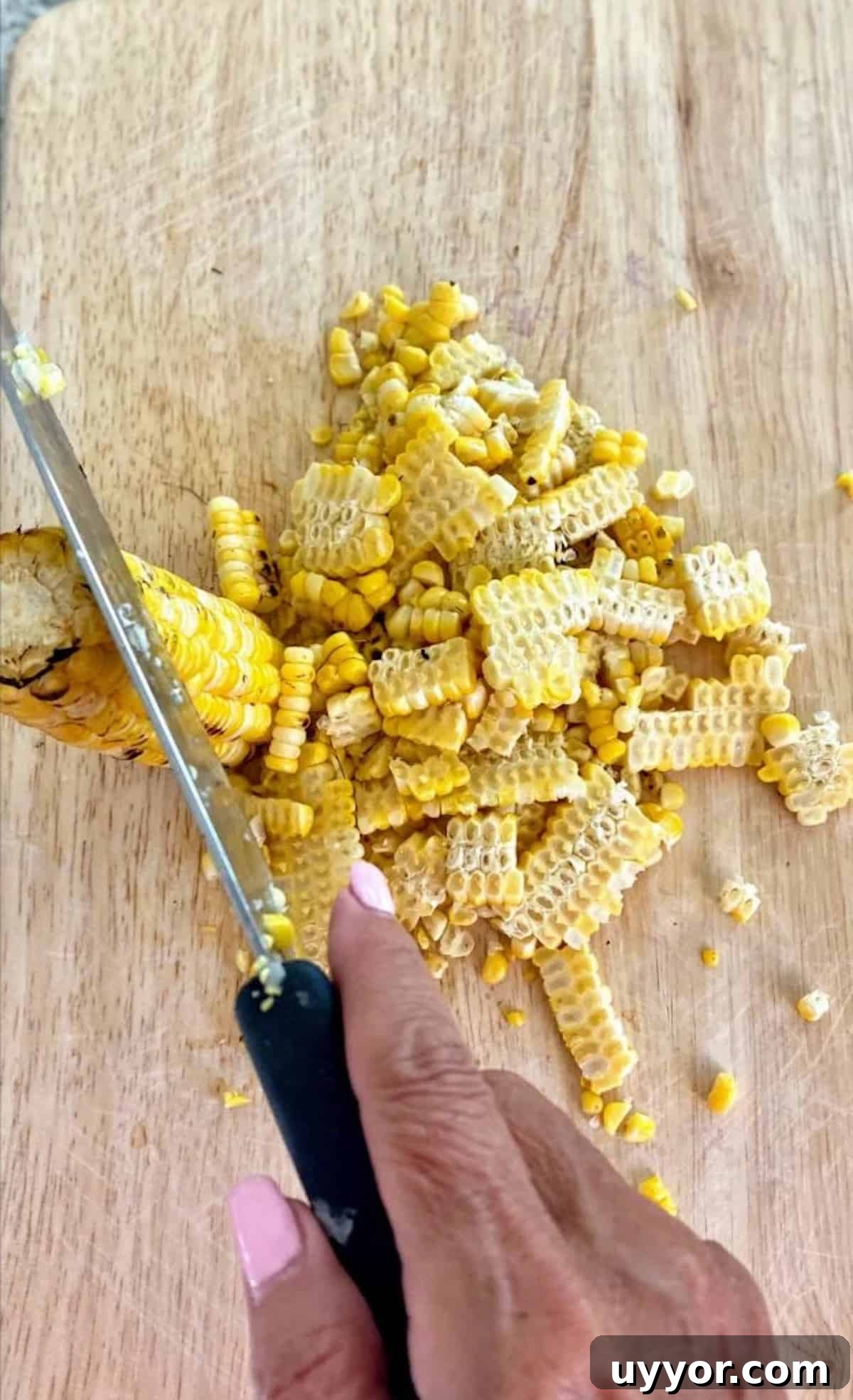 I am cutting grilled corn off the cobs on a cutting board.