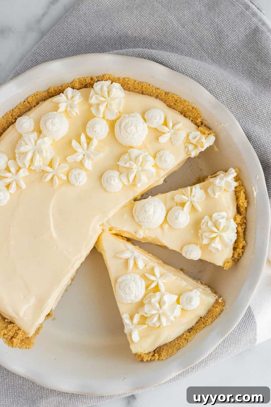 Lemon Cream Pie with Golden Oreo Crust: Zesty No-Bake Dessert 3 lemon cream pie with whipped cream decorations in white pie dish with 2 slices cut from pie
