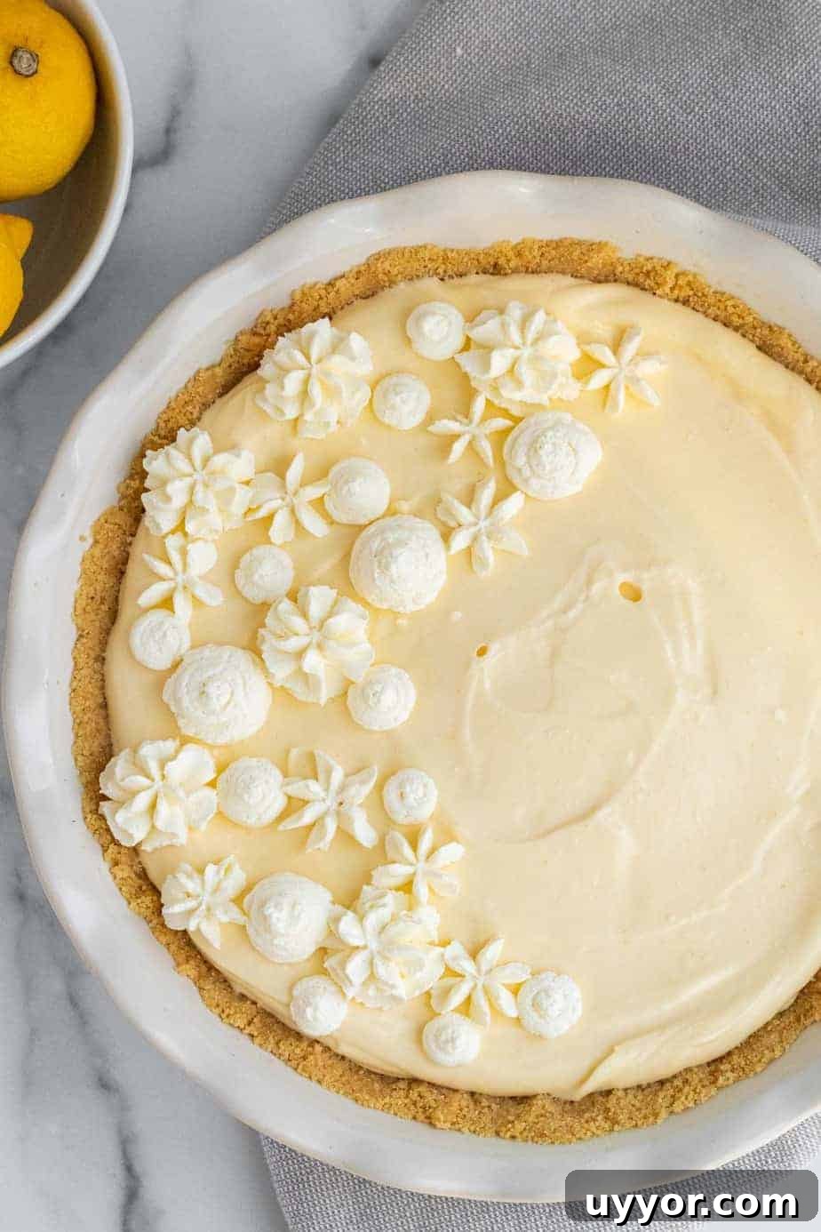 Lemon Cream Pie with Golden Oreo Crust: Zesty No-Bake Dessert 6 lemon cream pie in a white pie dish next to bowl of lemons