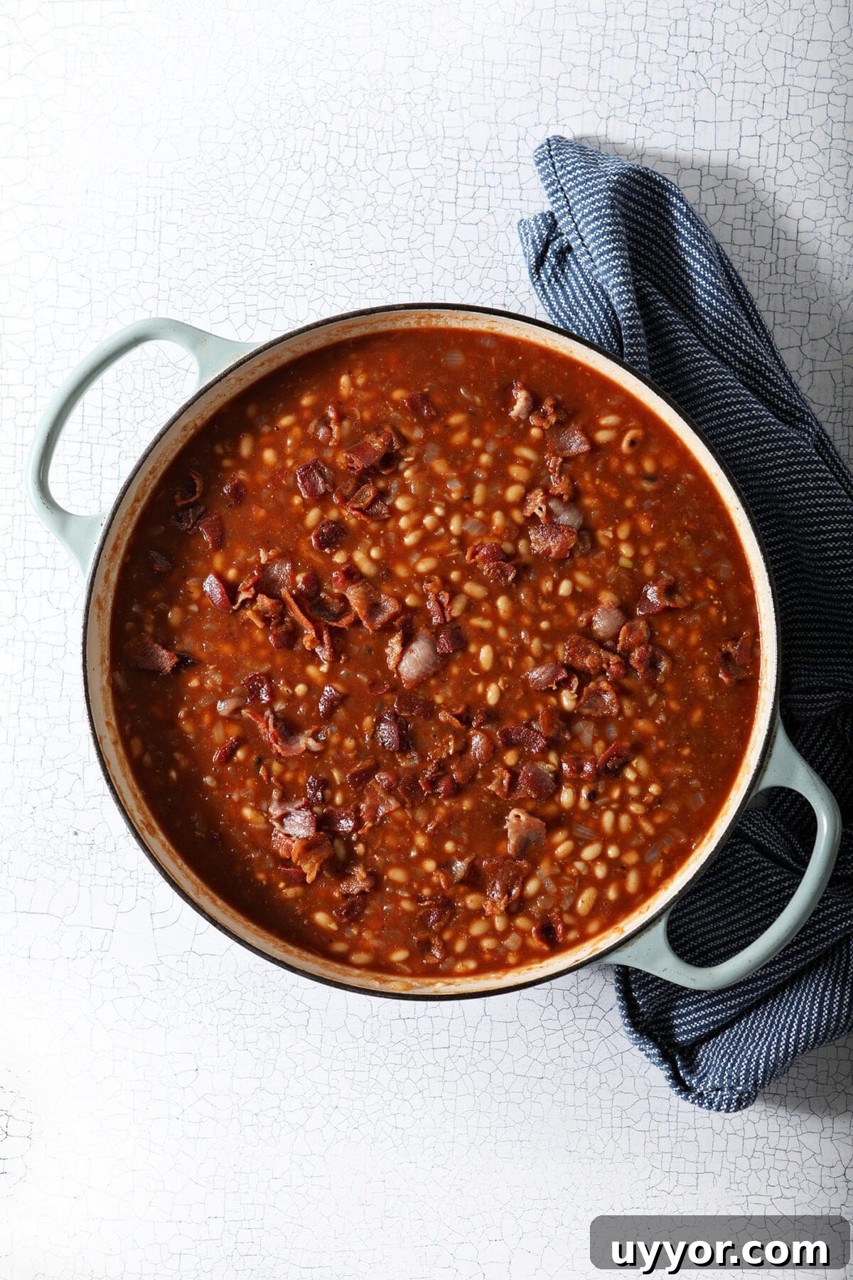 Overhead of baked beans in a pan before baking with bacon crumbles on top