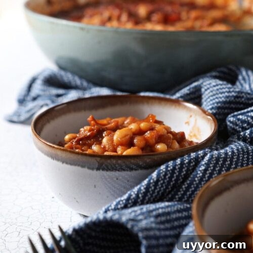 Two bowls of baked beans on a white tabletop with a blue striped towel