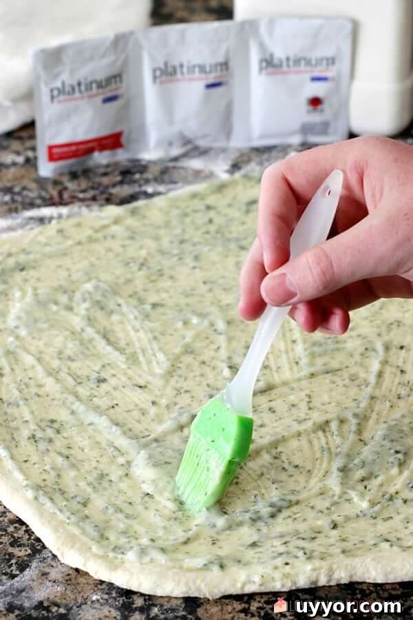 Cheesy Garlic Bread "Cinnamon" Roll dough being basted with butter sauce.