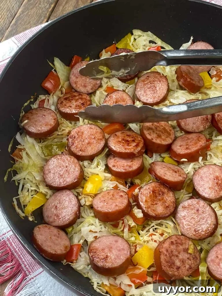 Savory Kielbasa and Cabbage Skillet Recipe for Weeknight Dinners 4 Tongs in cooked Kielbasa and cabbage