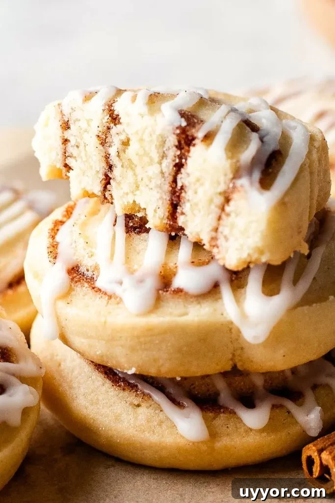 Cinnamon Roll Cookie Recipe: Soft Swirls with Cream Cheese Glaze 12 iced cinnamon roll cookies stacked on serving board with one cookie split in half