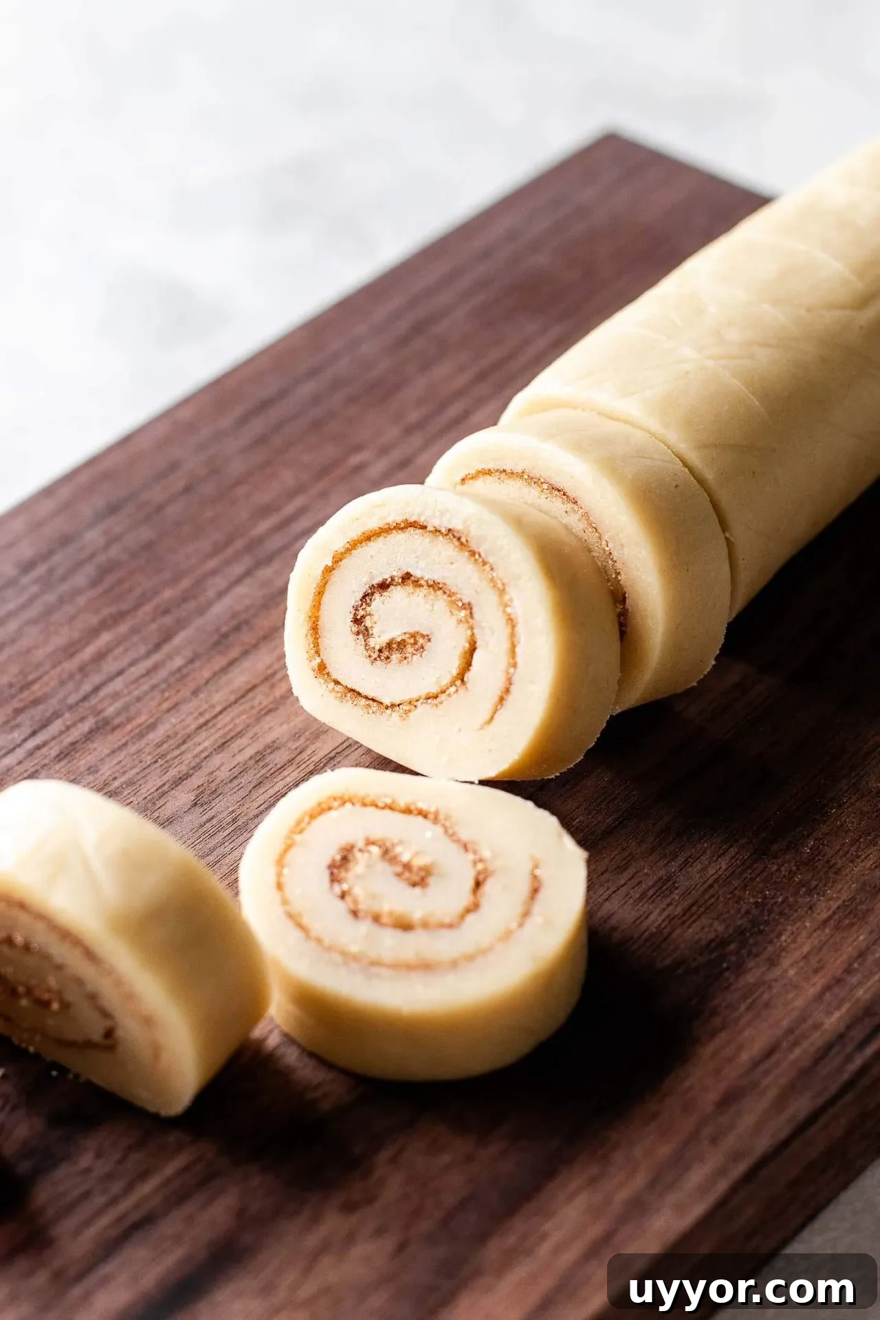 Cinnamon Roll Cookie Recipe: Soft Swirls with Cream Cheese Glaze 8 filled, rolled, and sliced cinnamon roll cookie dough on wooden cutting board