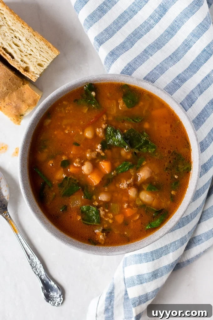 Instant Pot Ground Lamb Soup — Gluten-Free Recipe 2 A bowl of ground lamb stew on a white background with a blue striped towel, silver spoon, and focaccia bread.
