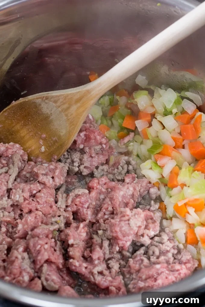 Instant Pot Ground Lamb Soup — Gluten-Free Recipe 4 Ground lamb and mirepoix being cooked in an instant pot and stirred with a wooden spoon.