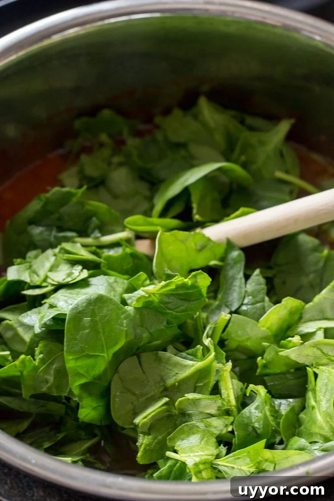 Instant Pot Ground Lamb Soup — Gluten-Free Recipe 7 Shredded spinach being added to soup in an instant pot.