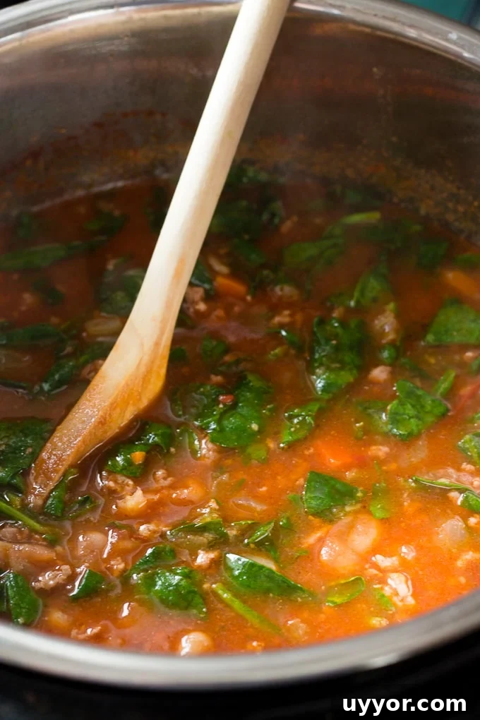 Instant Pot Ground Lamb Soup — Gluten-Free Recipe 8 Wilted spinach being stirred into a soup in an instant pot by a wooden spoon.