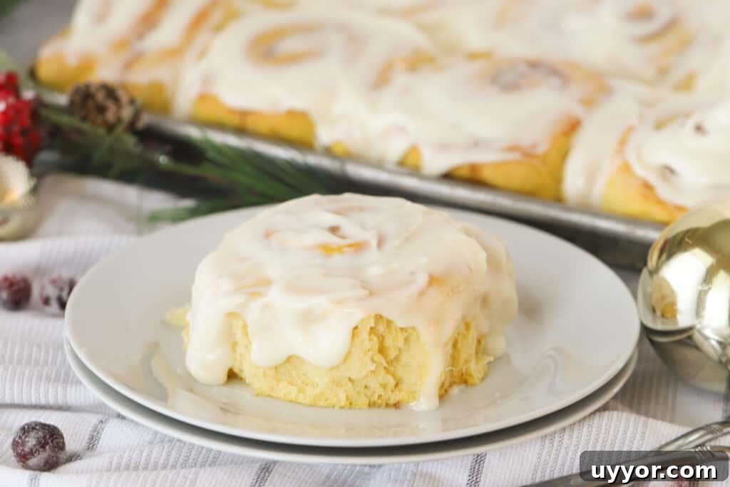 Zesty Lemon Sweet Rolls Recipe for Soft, Glazed Buns 3 A small white plate with a Lemon Sweet Roll covered in frosting and a full pan of sweet rolls in the background.